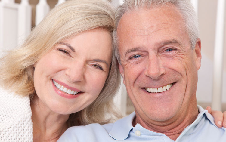 Stock image of an elderly couple smiling after receiving Implant-Supported Dentures.