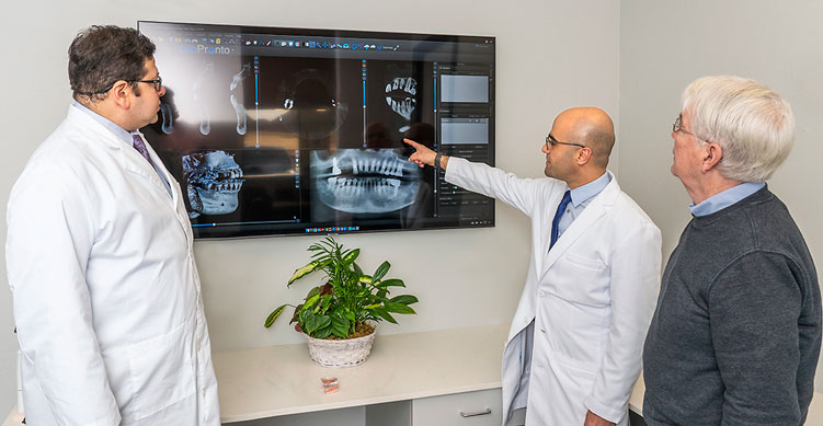 Image of a consultation with both Dr. Koticha and Dr. Al Sakka, showing a patient digital X-Rays to plan Dental Implants treatment.