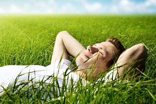 Stock image of a man lying in a field of grass, looking relaxed.