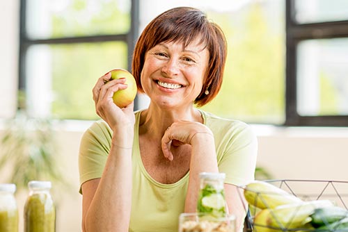 Stock image of a woman preparing to eat an apple after her Full-Mouth Rehabilitation treatment.