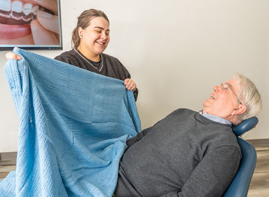 Image of a dental assistant making a patient comfortable in a dental chair by giving them a blanket.